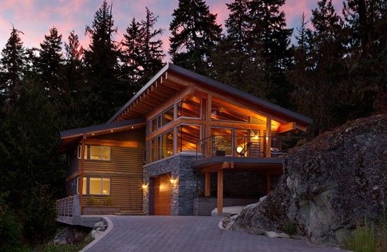 A Pacific Northwest home with a sloped roof, stone accents, warm windows, and pine trees